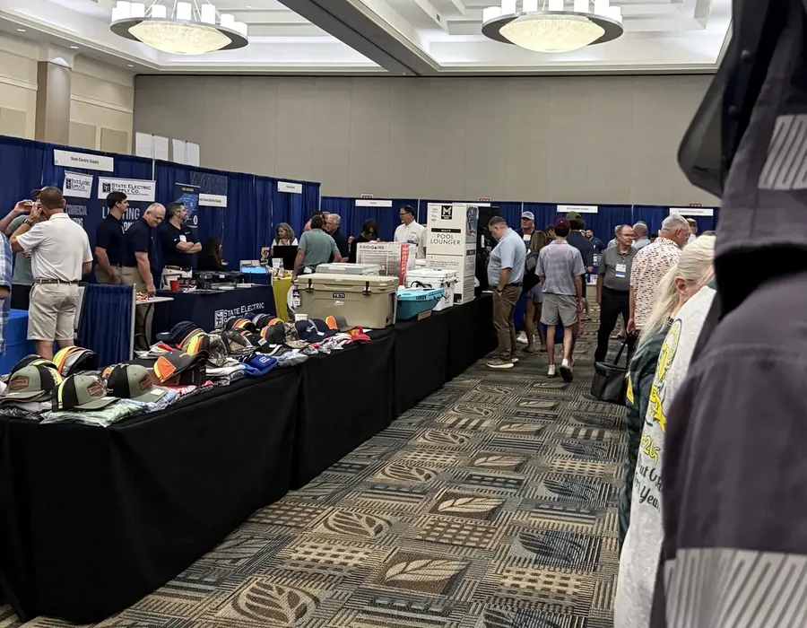 A busy NCAEC trade show floor framed by electrical safety gear and active exhibitor booths