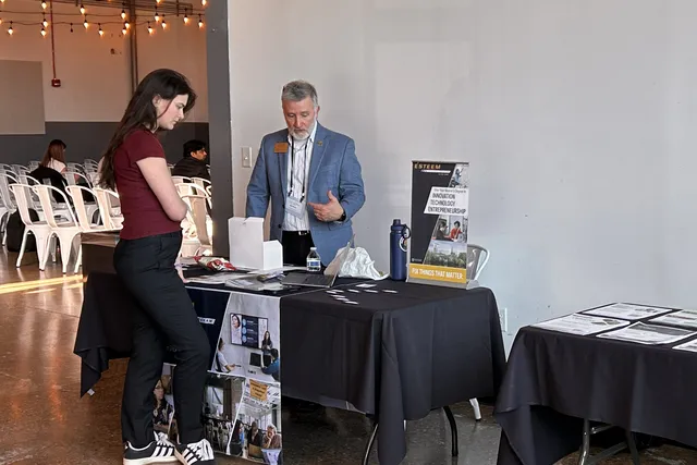 An exhibitor speaking with an attendee at the Intercollegiate Entrepreneurship Summit